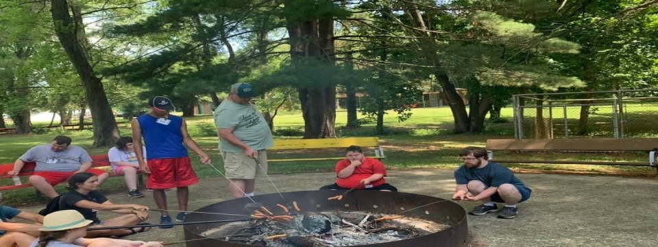 Campers cooking hotdogs over fire pit